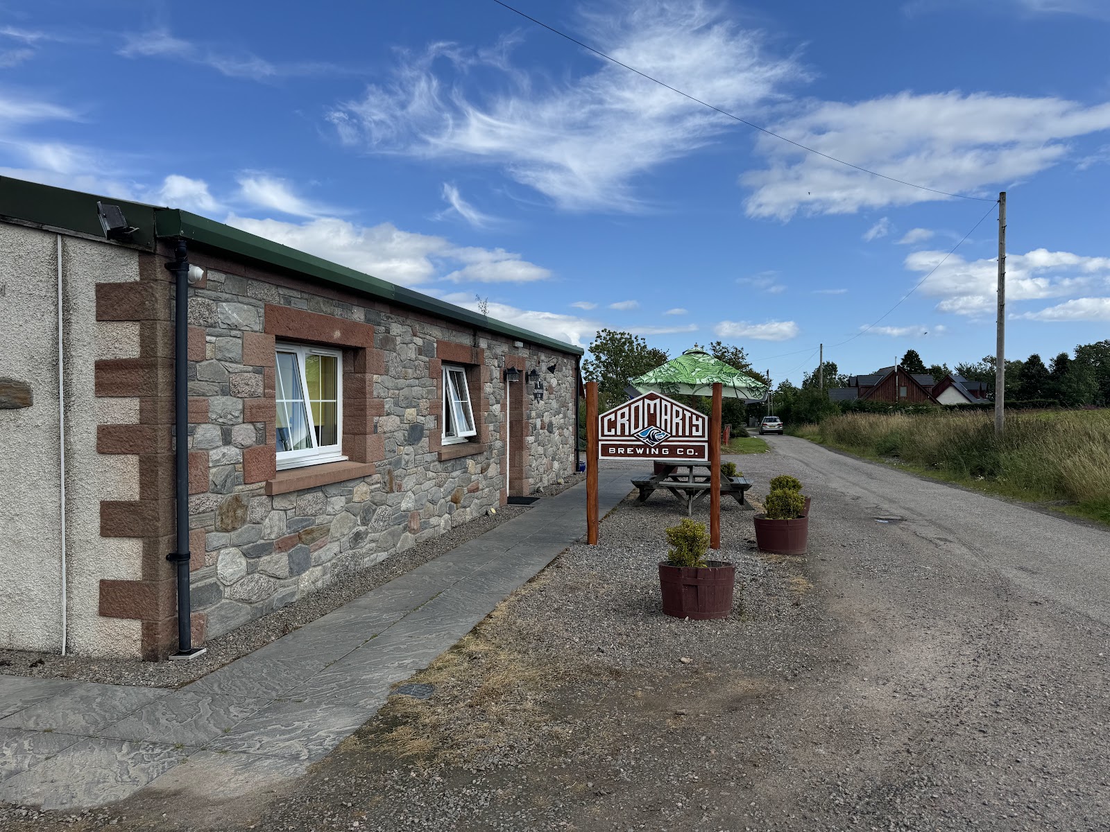 The Cromarty Brewing Company's stone building and painted sign beside a lane at Davidston, under a blue sky.