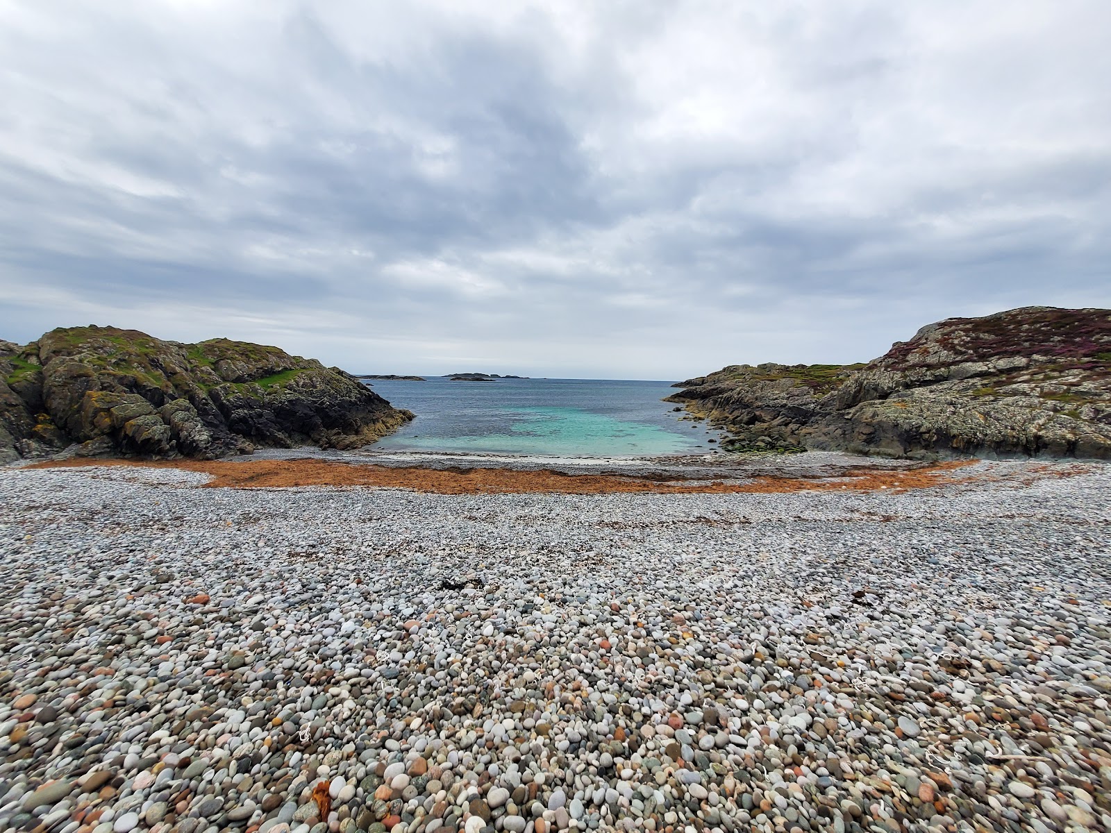 The pebble beach of St Columba's Bay on Iona between rocky outcrops, the sea beyond.