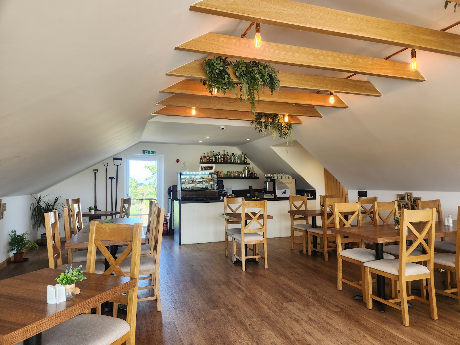 The restaurant at Puldagon Farm, wooden tables and chairs under timber beams hung with greenery.