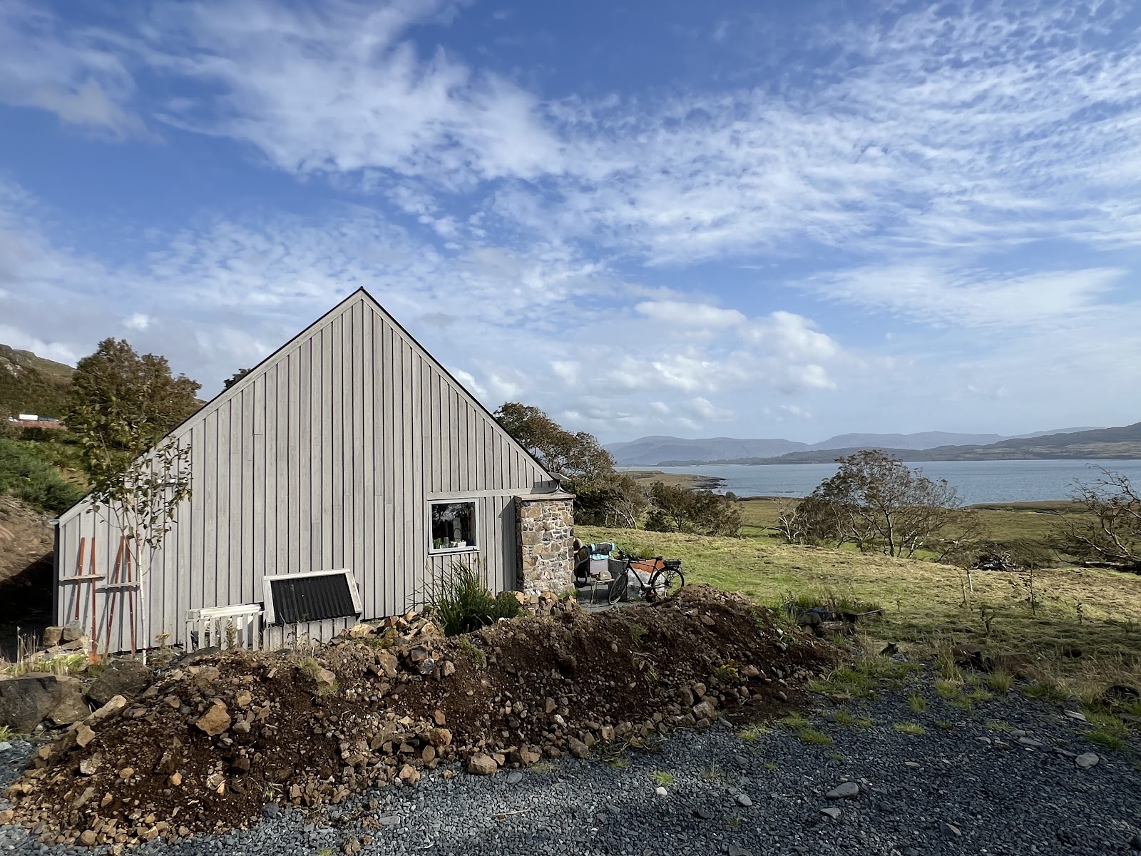 The pale timber building of Croft 3 on the croft, the sea and hills behind.