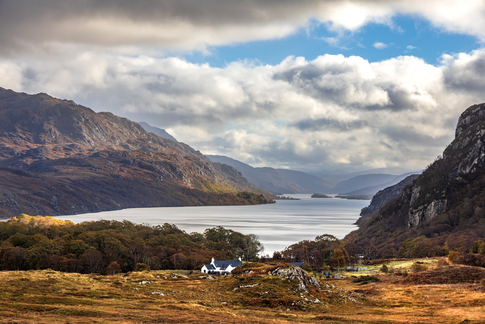White cottage below a Highland loch flanked by autumn hills