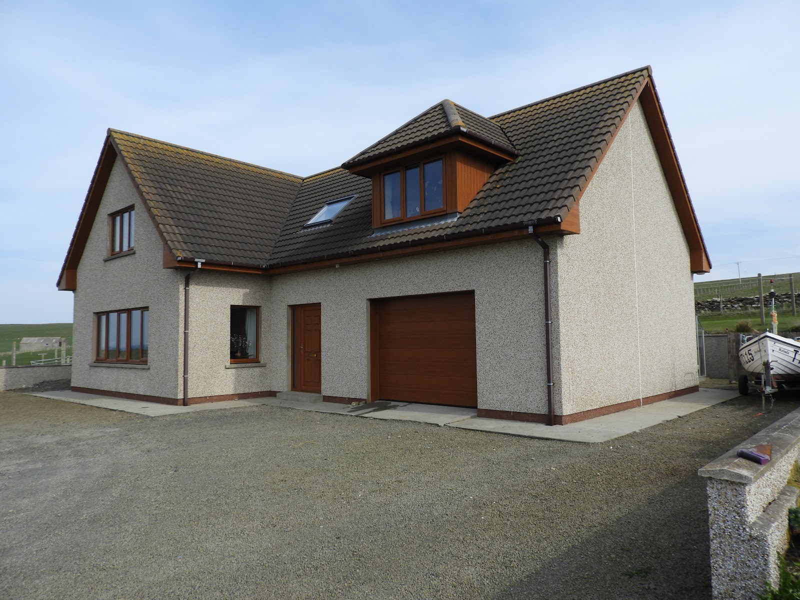 Pebble-dashed dormer bungalow with wooden garage door and gravel driveway