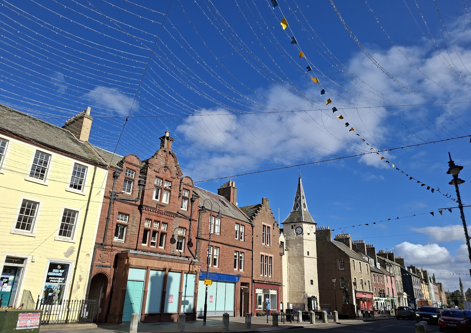Dunbar High Street under a blue sky, the white Town House with its tower and spire among the old buildings.