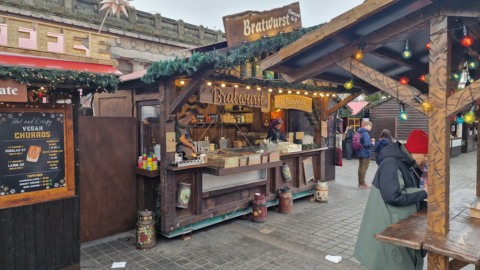 Wooden chalets of the Christmas market in East Princes Street Gardens, hung with greenery and signs.