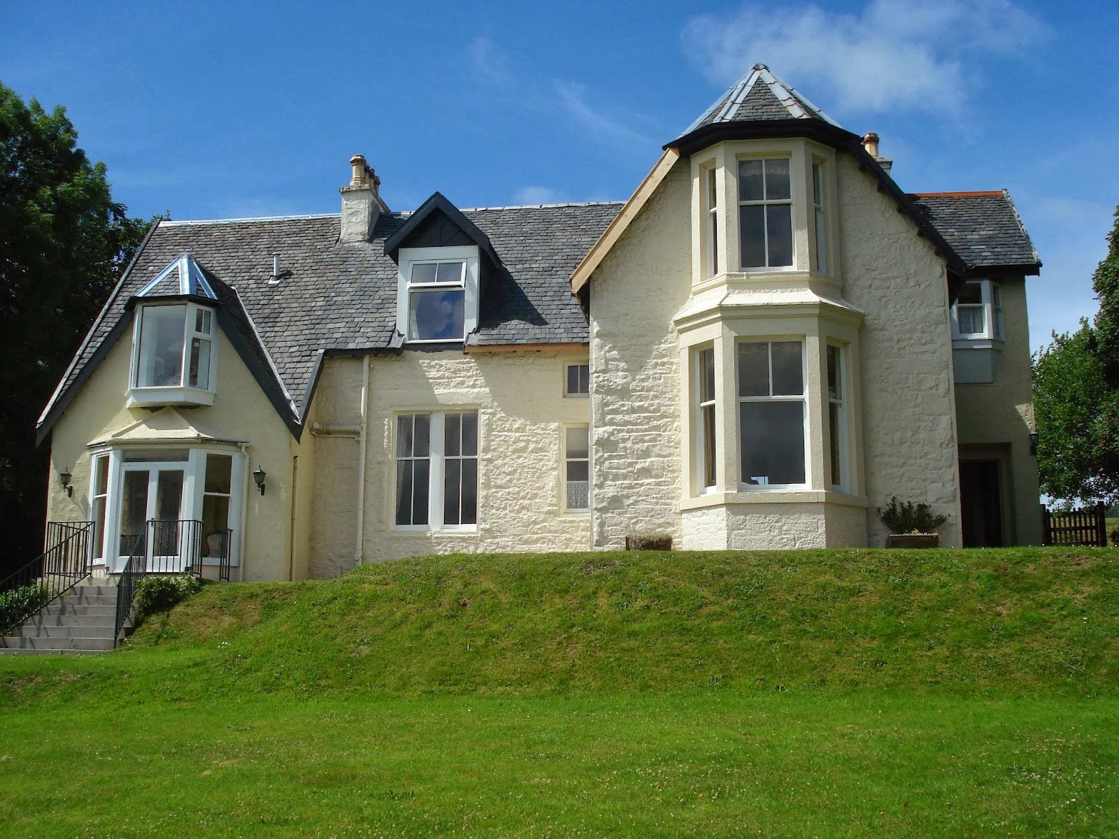 Victorian villa with bay windows and turret roof, set above a sloping lawn
