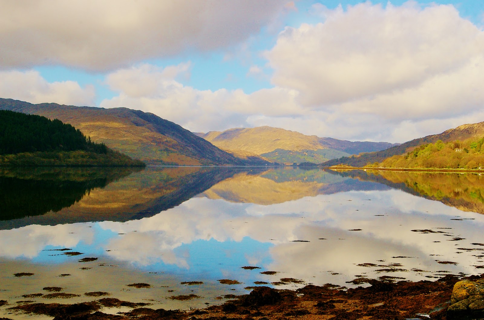Loch Sunart, still water perfectly reflecting autumn hills and a cloud-scattered sky.