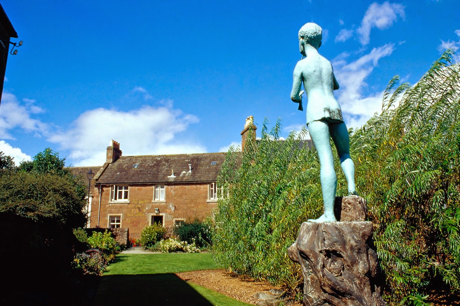 A verdigris statue overlooks a walled garden and sandstone house