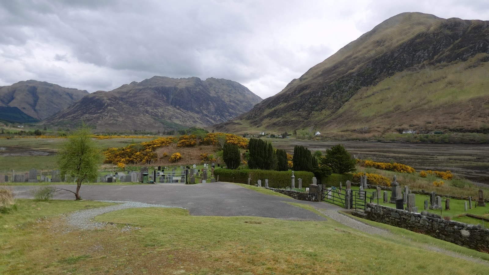 Gravestones and gorse bushes below mountains flanking a wide glen