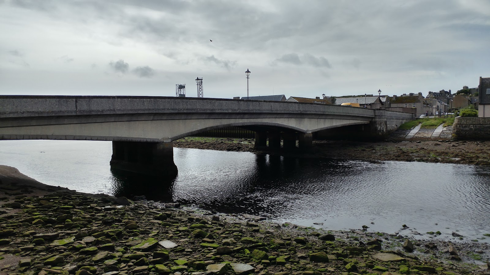 Concrete road bridge spanning a tidal inlet lined with seaweed-covered rocks