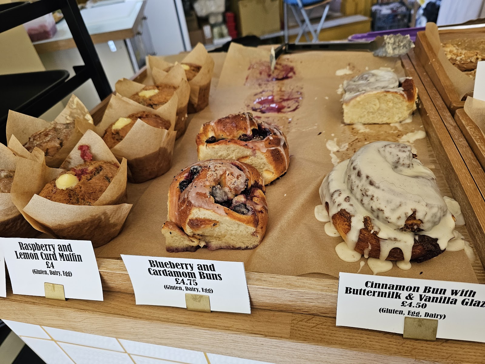 The counter at Jeannie's Bakery, with muffins, blueberry and cardamom buns and a glazed cinnamon bun on brown paper above their labels.