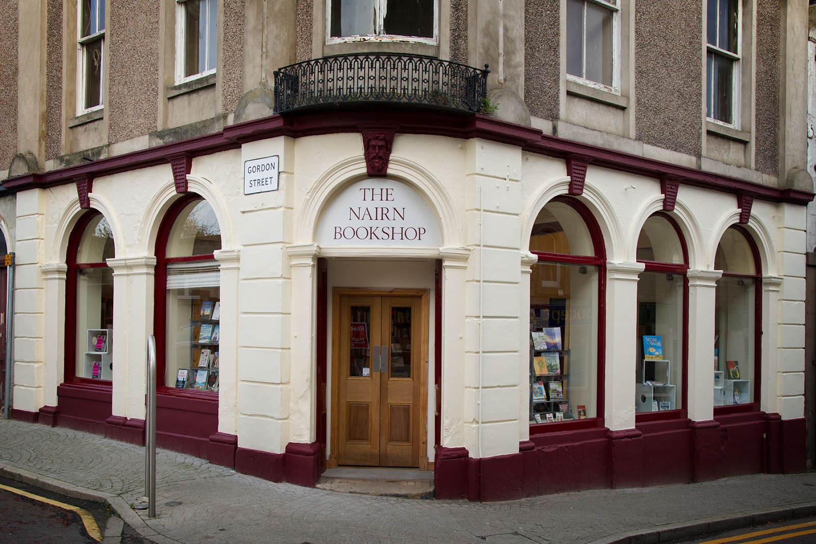 The Nairn Bookshop on the corner of the High Street and Gordon Street, a cream and maroon front with arched windows and wooden double doors.