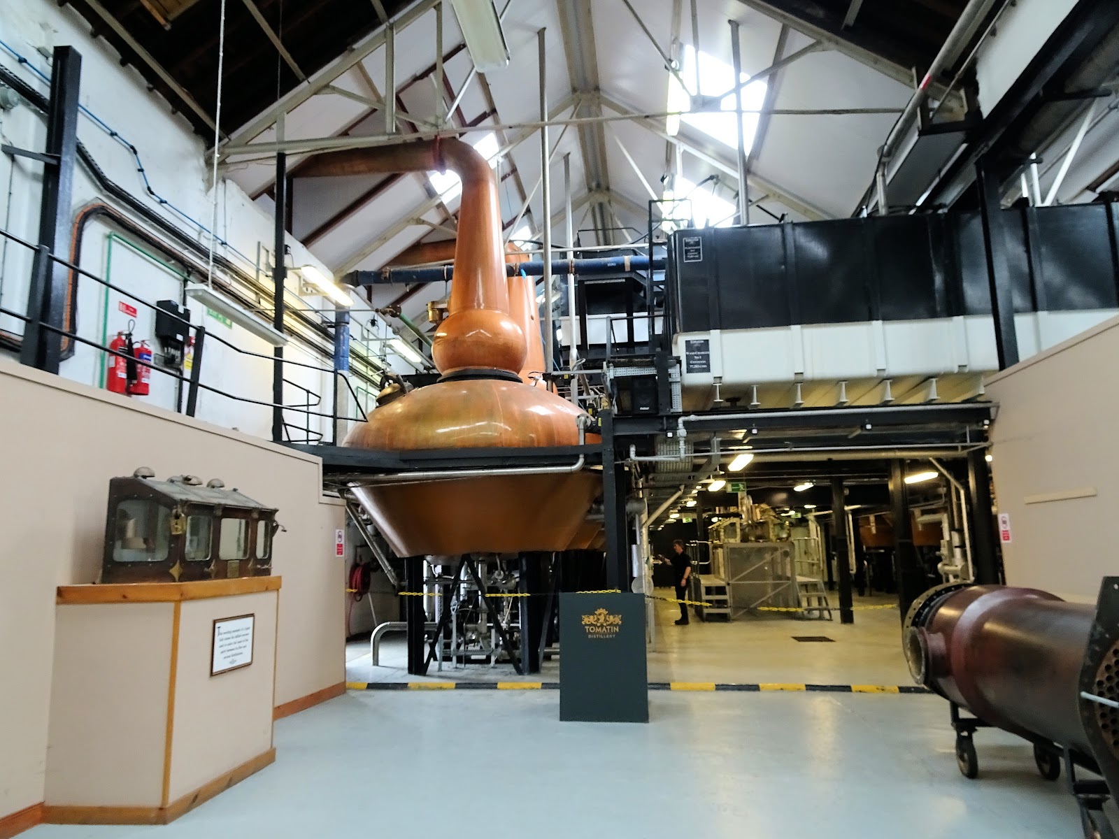 Tomatin's stillhouse, a copper pot still under a high steel roof, with pipework and walkways behind.