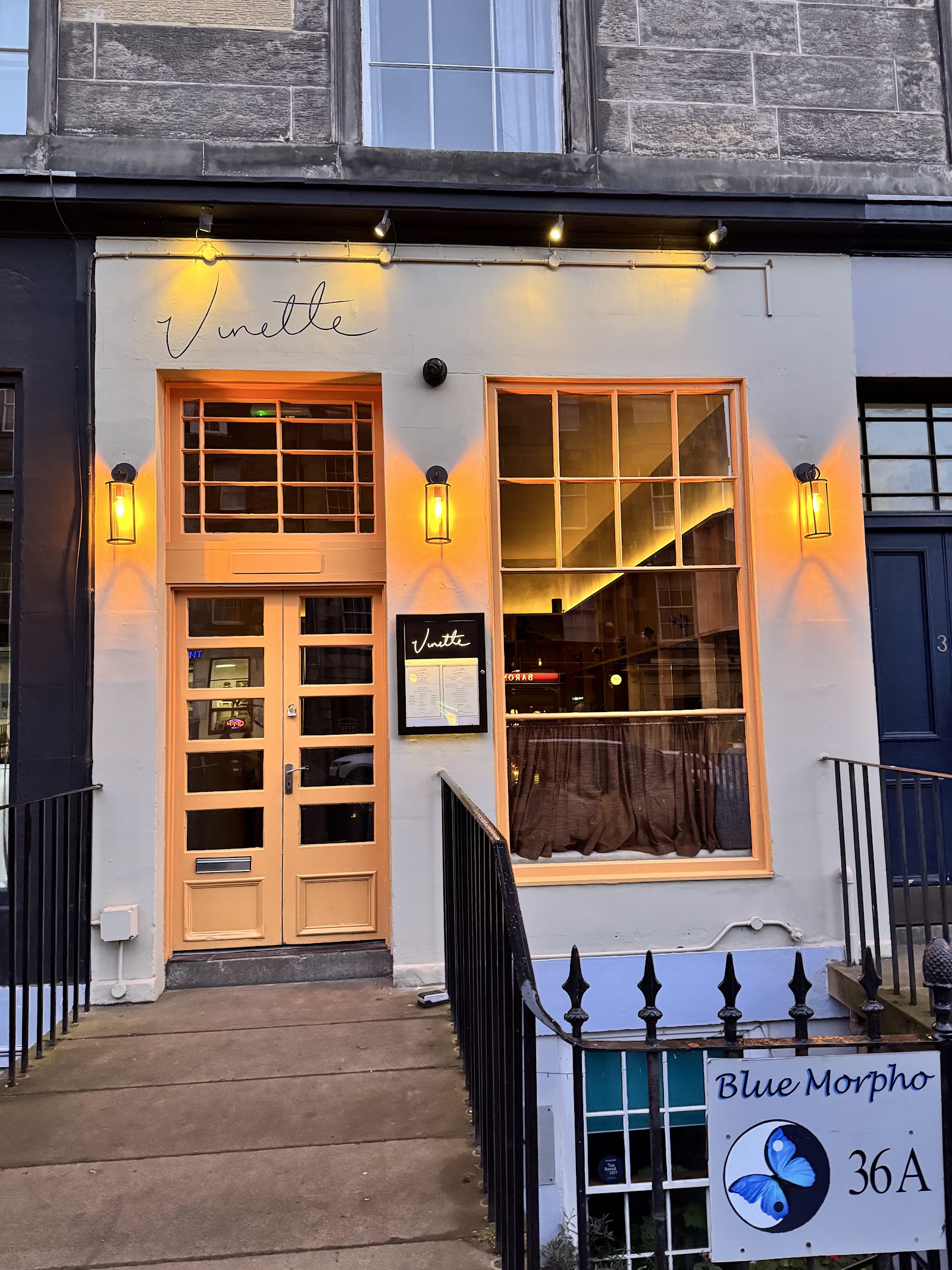 Vinette's pale front on Broughton Street at dusk, its name above the apricot door and tall window, with lamps lit either side.
