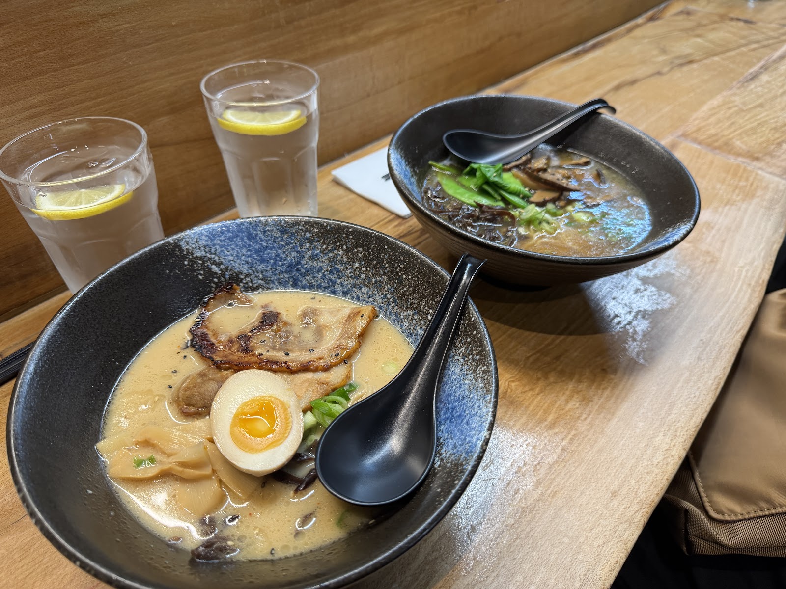 Two bowls of ramen at Ikigai on South Bridge: a creamy tonkotsu with pork belly and a soft egg, and a dark mushroom broth, by glasses of water with lemon.