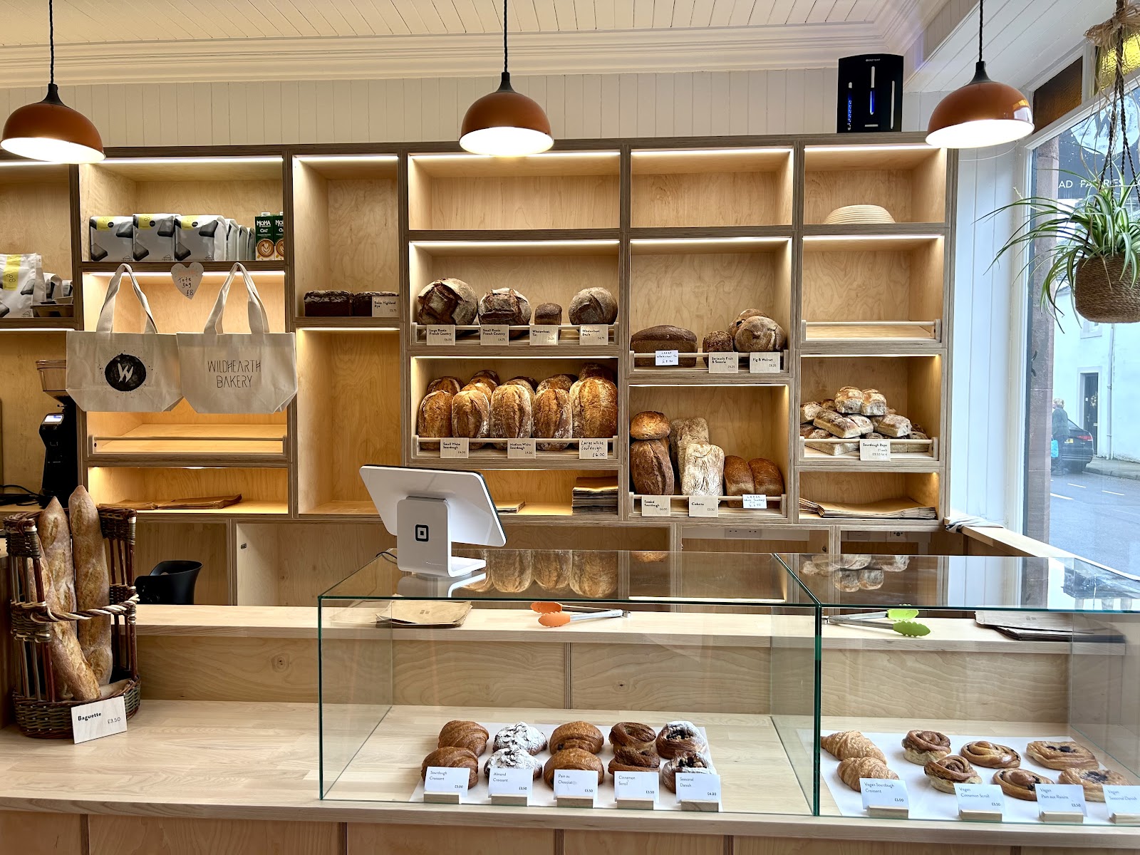 The Wild Hearth Bakery shop in Comrie, with sourdough loaves on wooden shelves behind a glass counter of pastries and cinnamon buns.