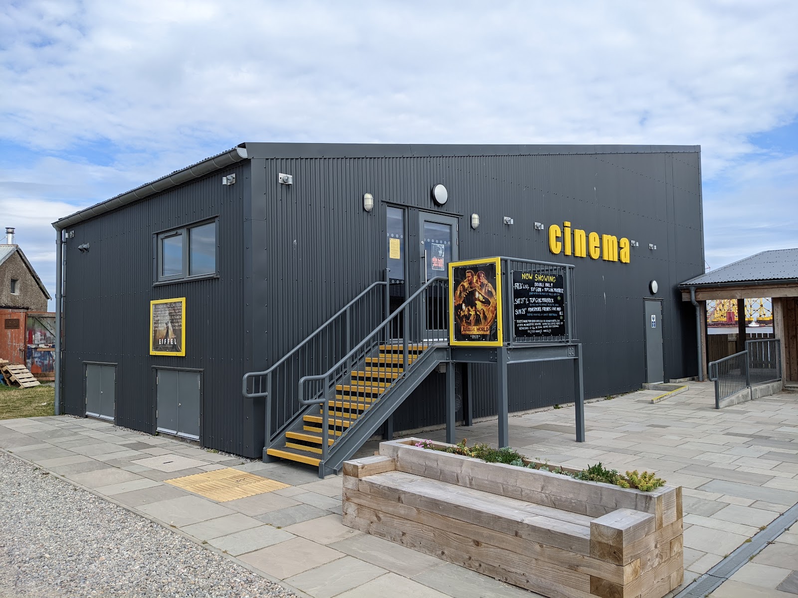 Cromarty Cinema, a dark modern building lettered cinema in yellow, with an outside stair, beside the harbour.