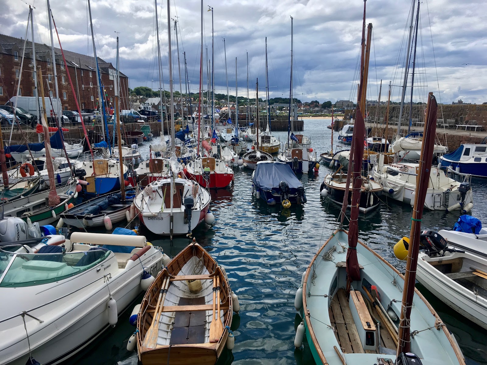 North Berwick harbour, small boats and yachts moored close together below old stone buildings.
