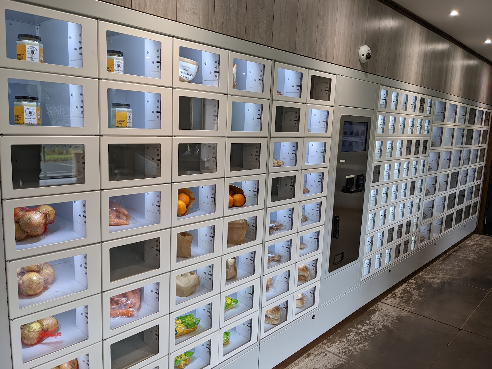 The wall of glass-fronted vending lockers inside Thorneybank Farm Shop, filled with onions, carrots, oranges, rolls and jars of honey.