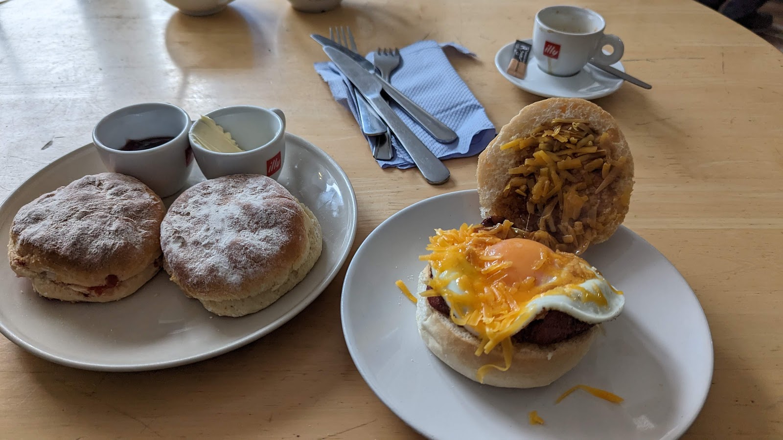 A breakfast roll with fried egg and cheese and two scones with jam and butter on a table at Preacher's Patisserie.