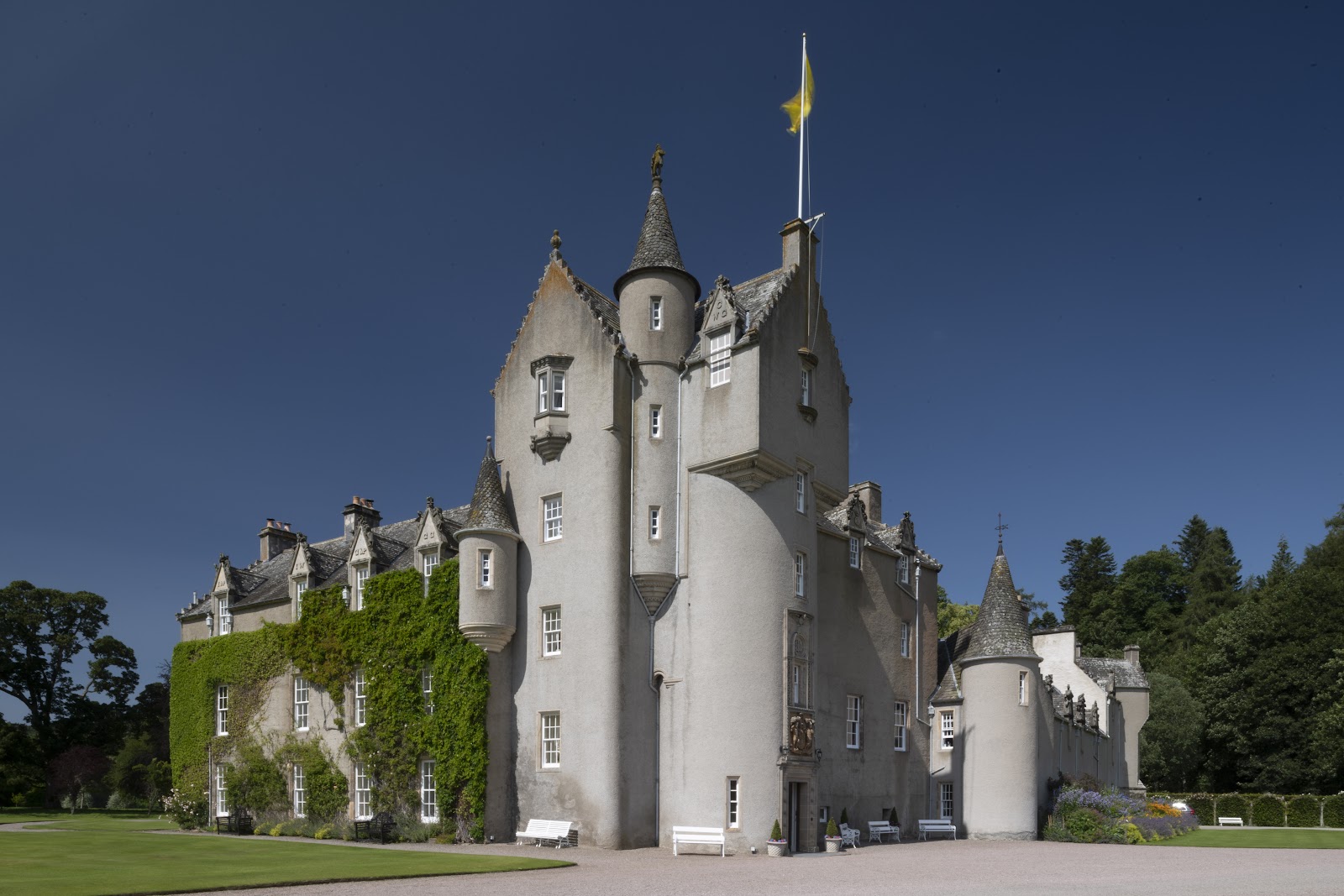 Ballindalloch Castle, a white tower house with turrets and ivy on its lower walls, under a deep blue sky.