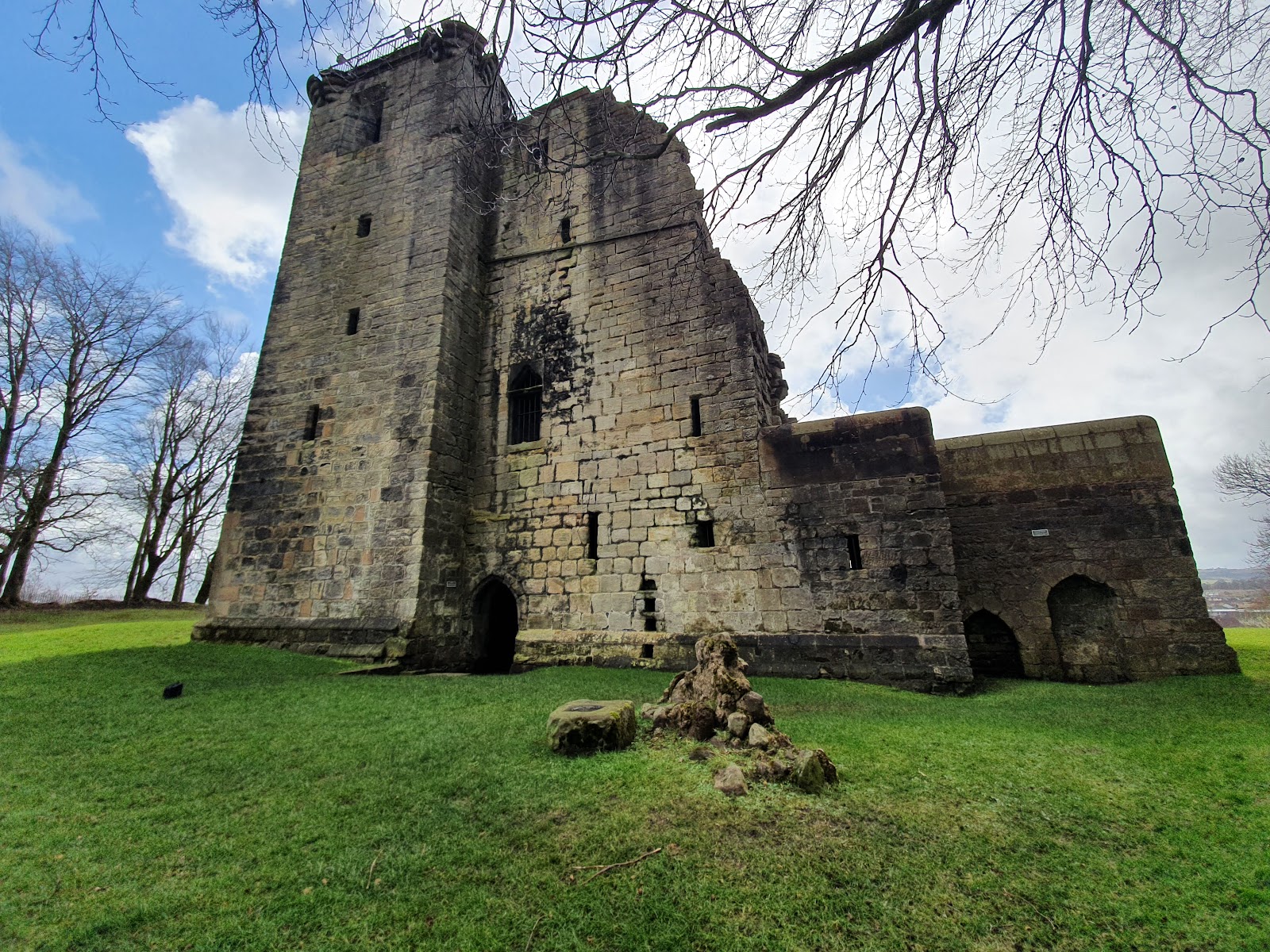 Crookston Castle from the grass, its ruined tower and lower walls under bare branches and a bright sky.