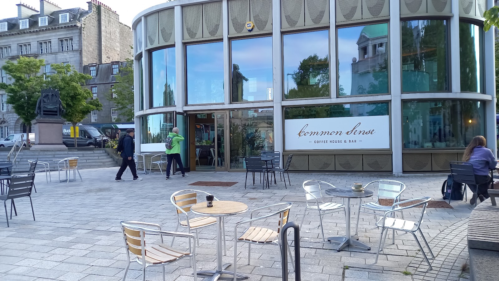 The glass pavilion of Common Sense Coffee House and Bar on the terrace above Union Terrace Gardens, with tables outside.