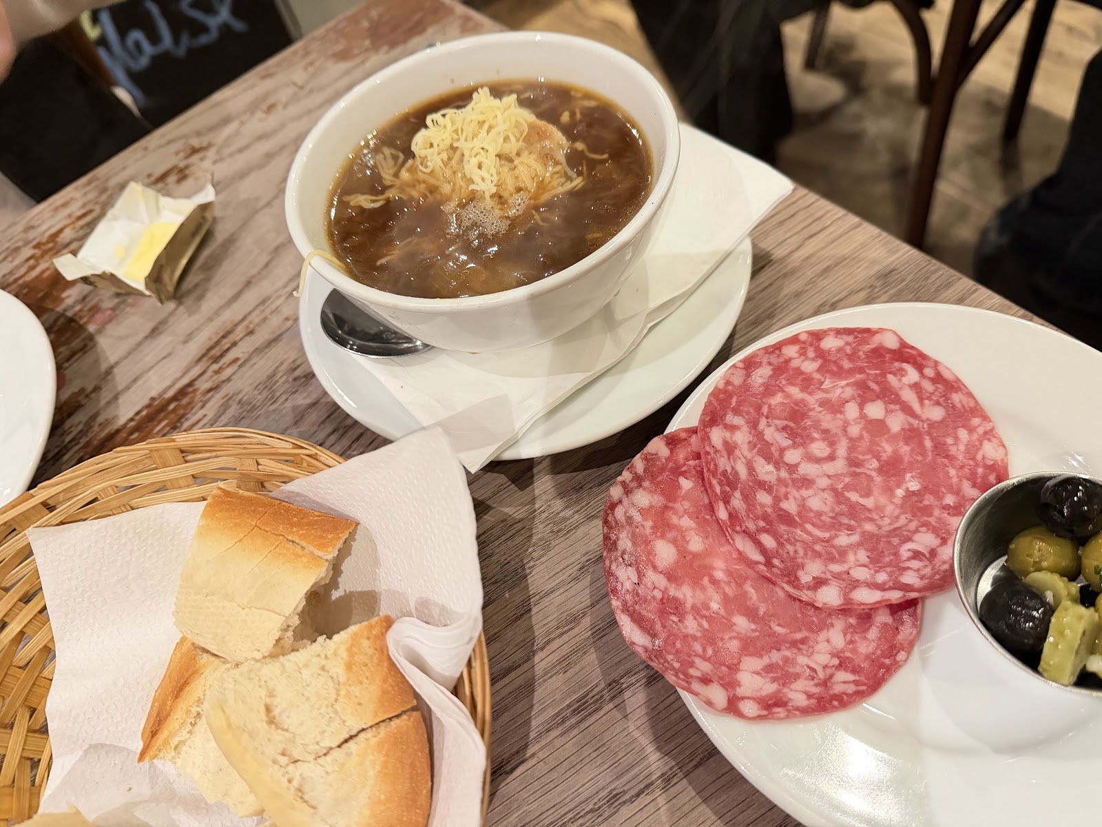 French onion soup topped with cheese, a basket of bread and slices of saucisson on a table at Chez Jules on Hanover Street.