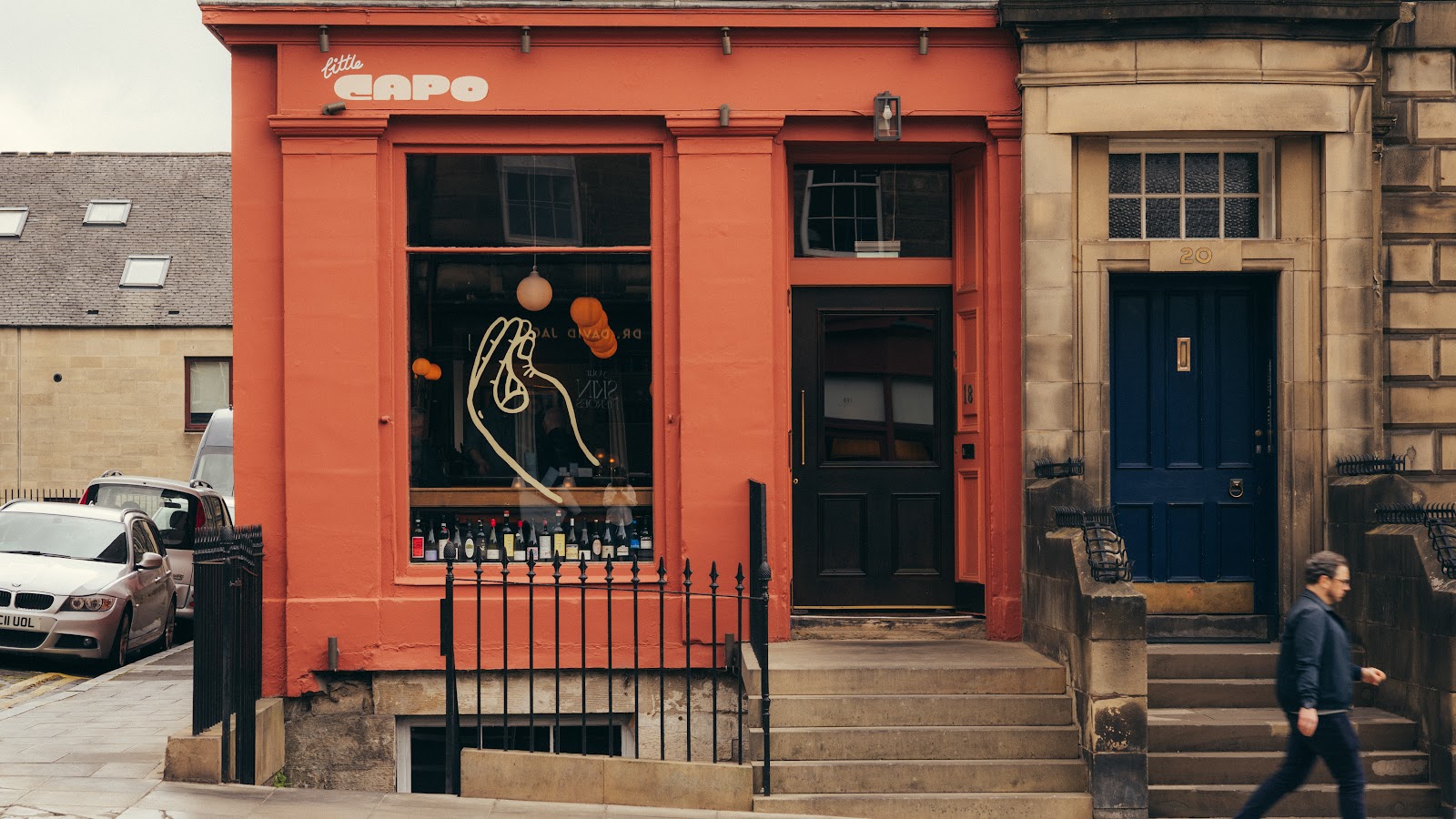 The salmon-pink front of Little Capo at 18 Howe Street, its name painted above a big window lined with wine bottles and a black door at the top of the steps.