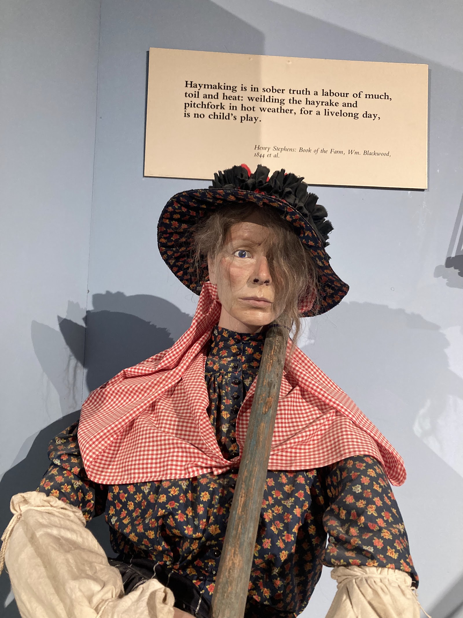 A costumed figure in a red gingham shawl and black bonnet among the displays of the Aberdeenshire Farming Museum.