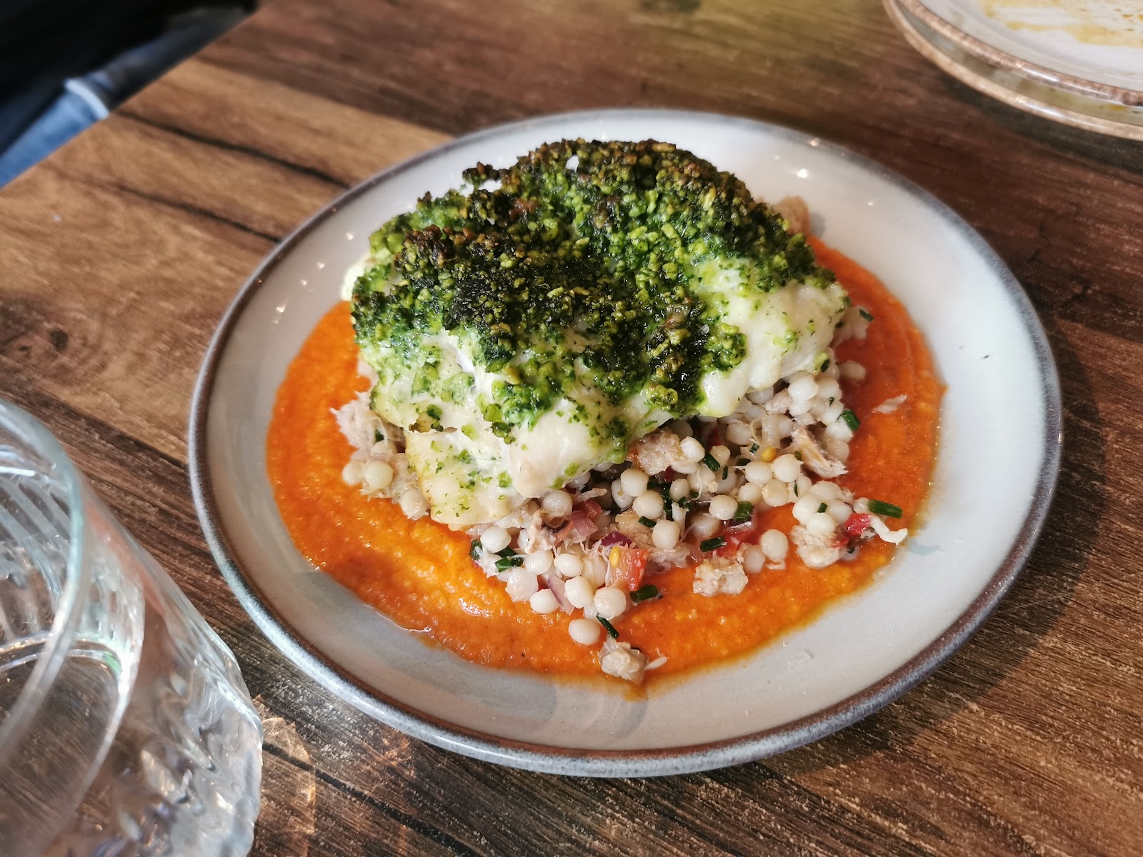 White fish under a green herb crumb on giant couscous and a red pepper sauce, on a table at Lobo.