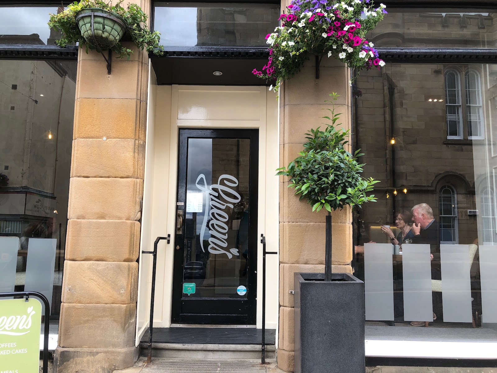 The front door of Greens at London House in Tain, lettered Greens, with hanging baskets of flowers above.