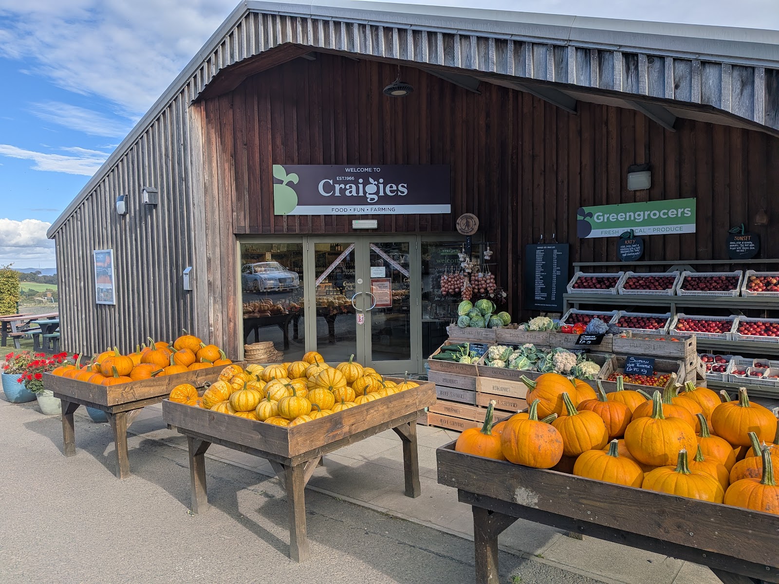 The timber front of the Craigies farm shop under a blue sky, with tables of pumpkins and crates of apples, cauliflowers and cabbages outside the door.
