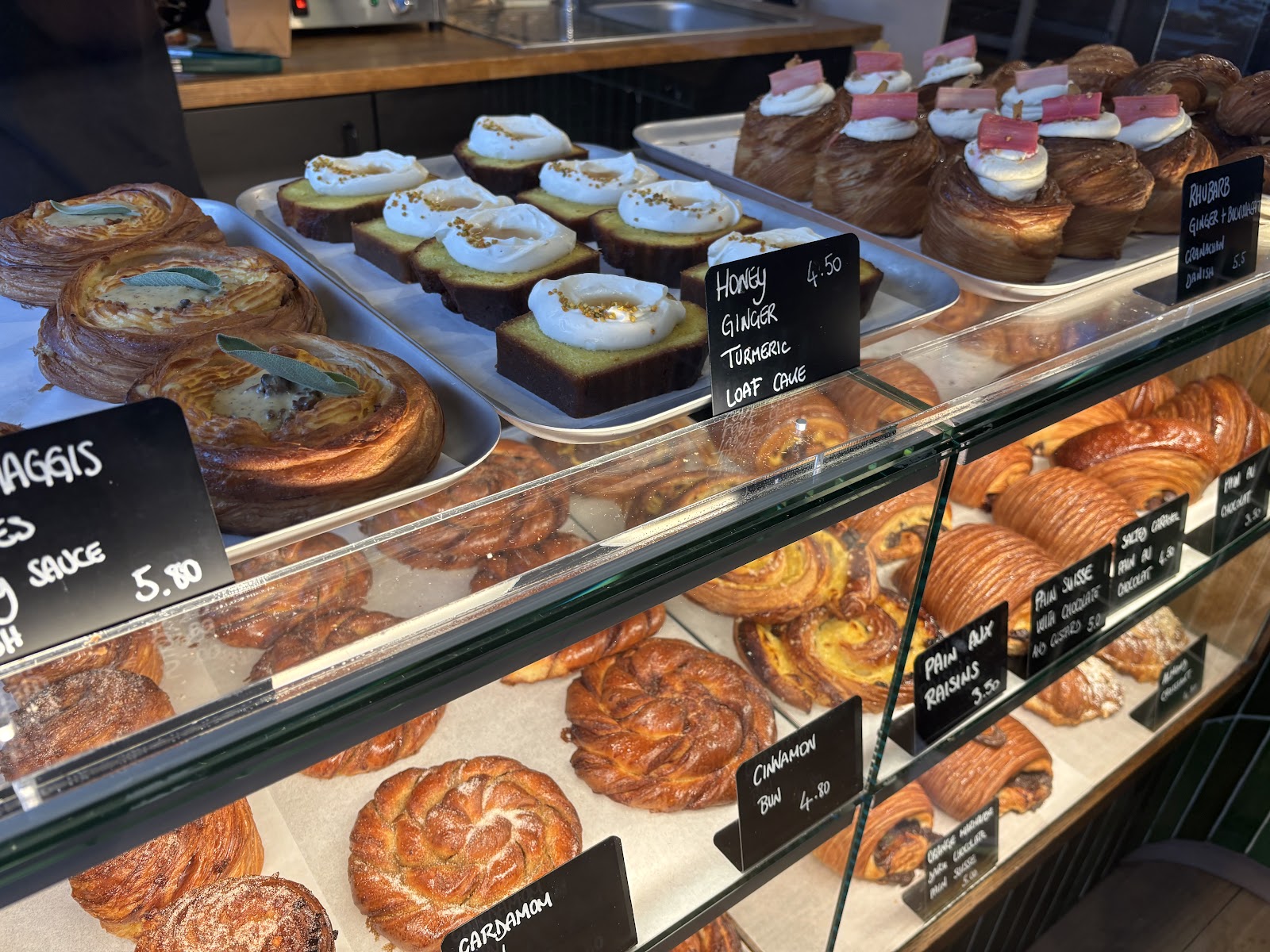 The counter at Sloe Lane Bakery, full of pastries, loaf cakes topped with cream and chalked labels.