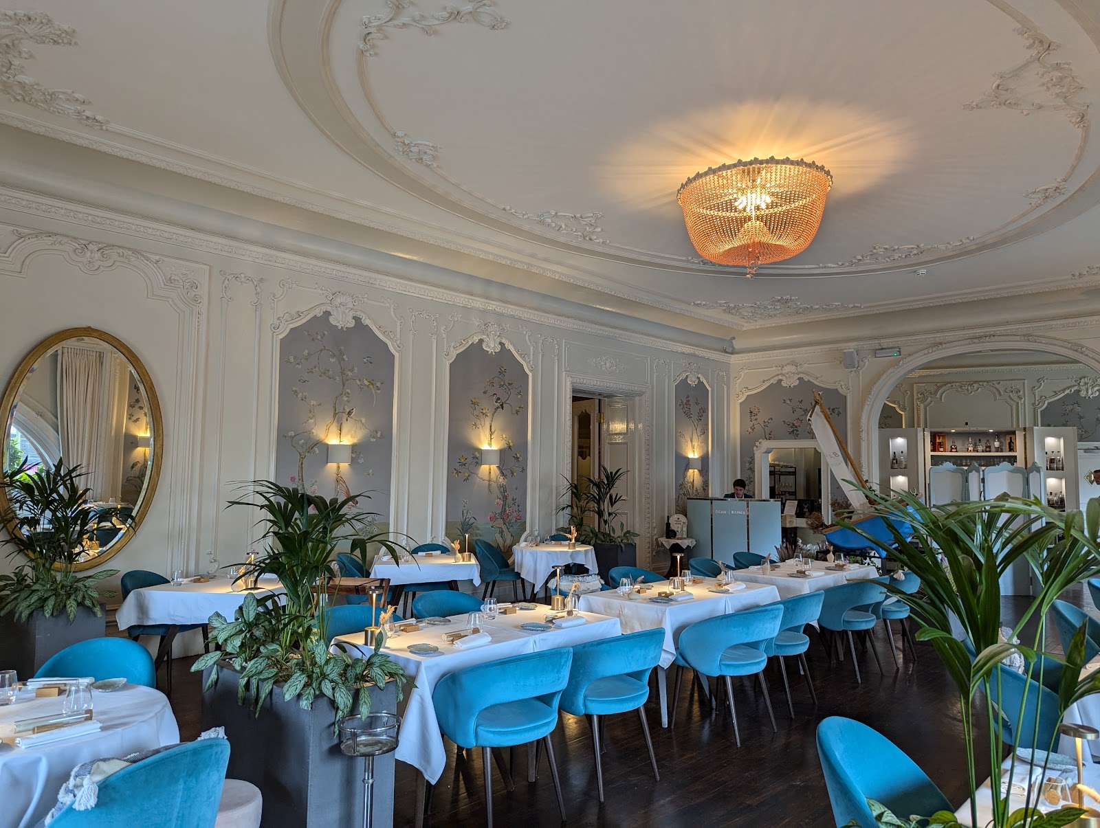 The Pompadour dining room in the Caledonian hotel, with white-clothed tables and turquoise chairs under an ornate plaster ceiling, painted wall panels and a gold-framed mirror.
