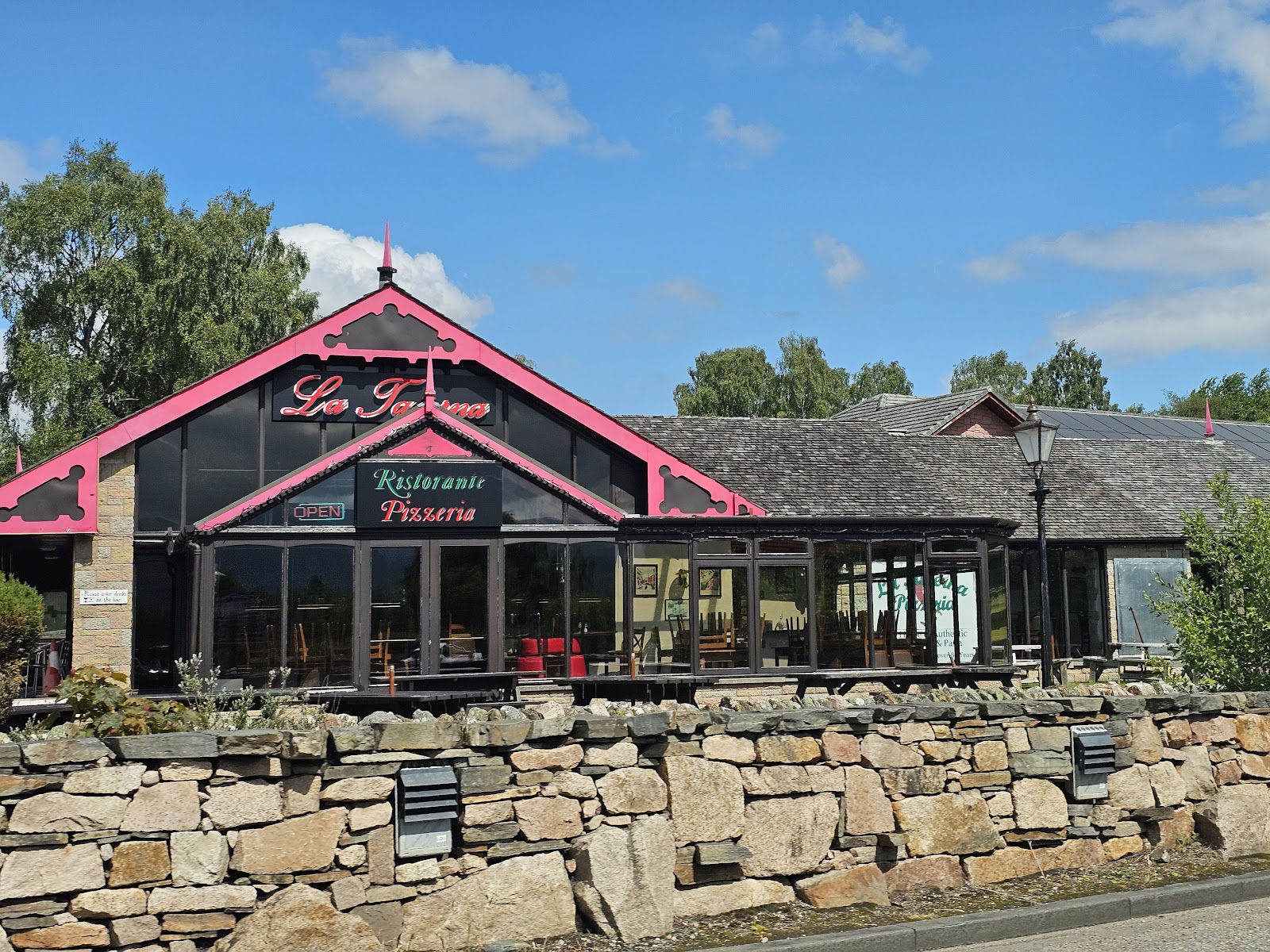 La Taverna's pink-gabled front and glass dining room behind a stone wall in Aviemore.