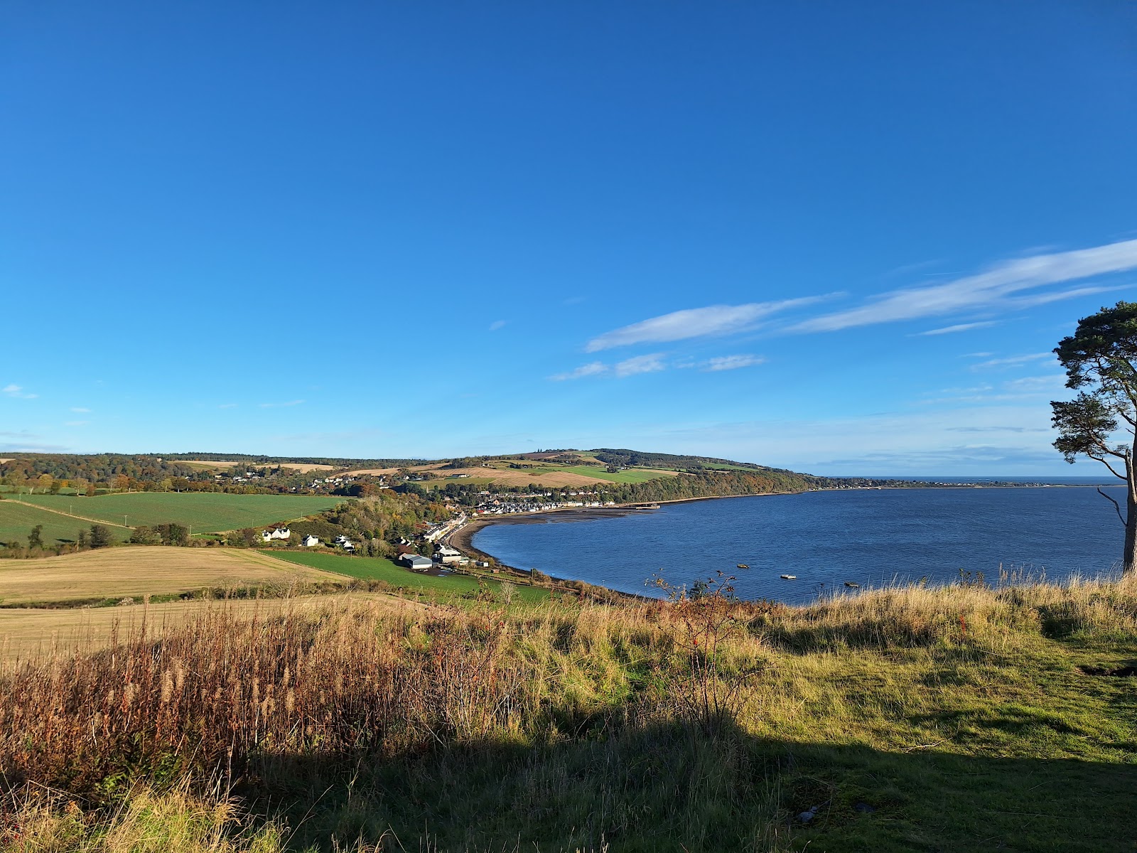 The view from Ormond Hill over Avoch Bay, golden fields and the shore of the Black Isle under a blue sky.