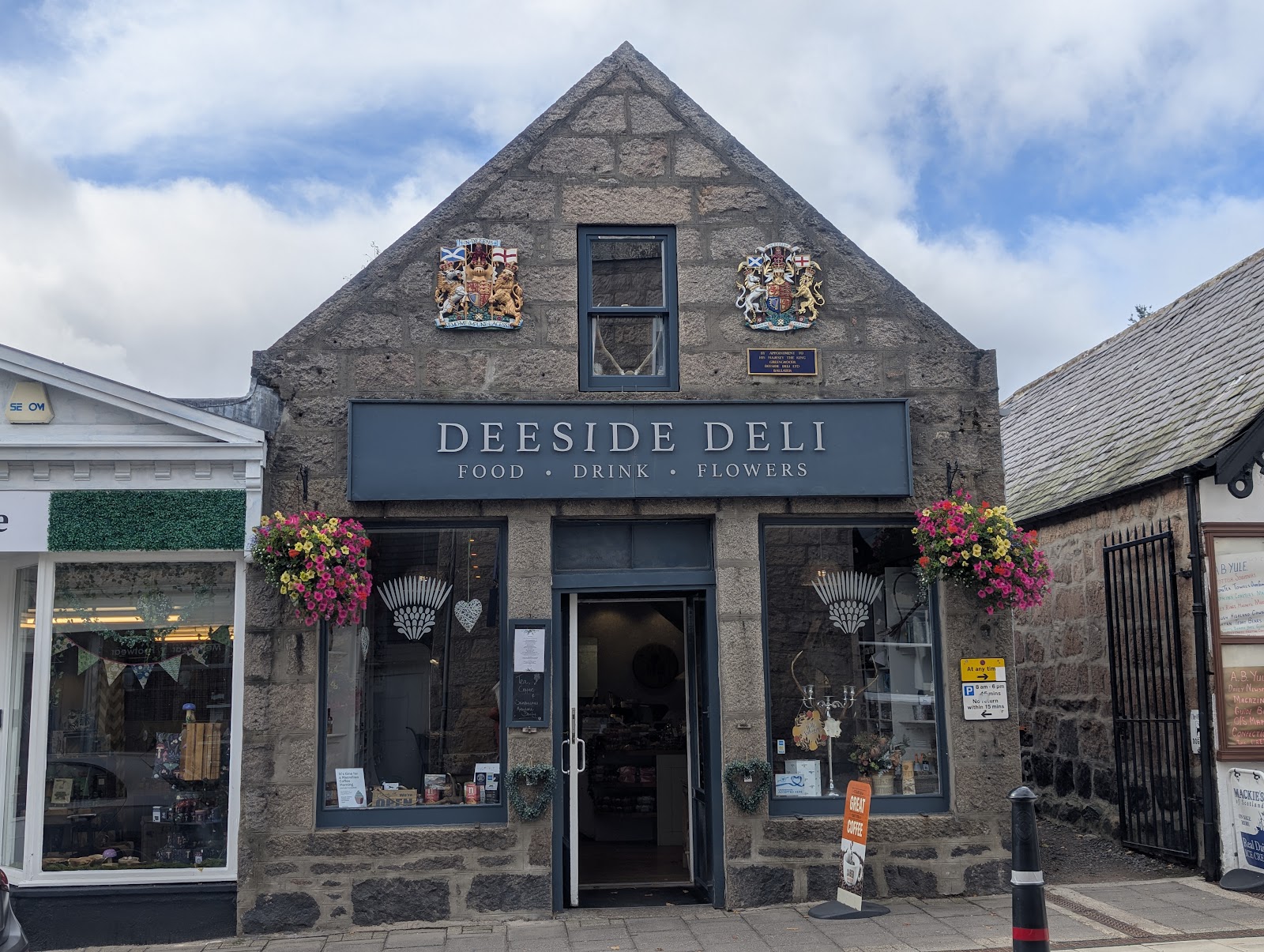 The granite front of the Deeside Deli on Bridge Street, Ballater, flowers hanging by its windows.