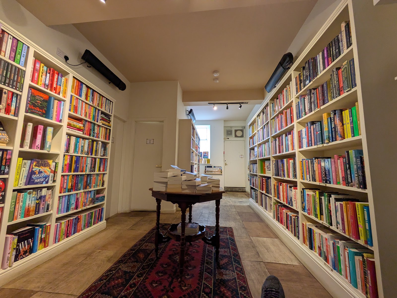 Inside BEINN in Dufftown, a long room lined with white shelves of books around a table on a rug.