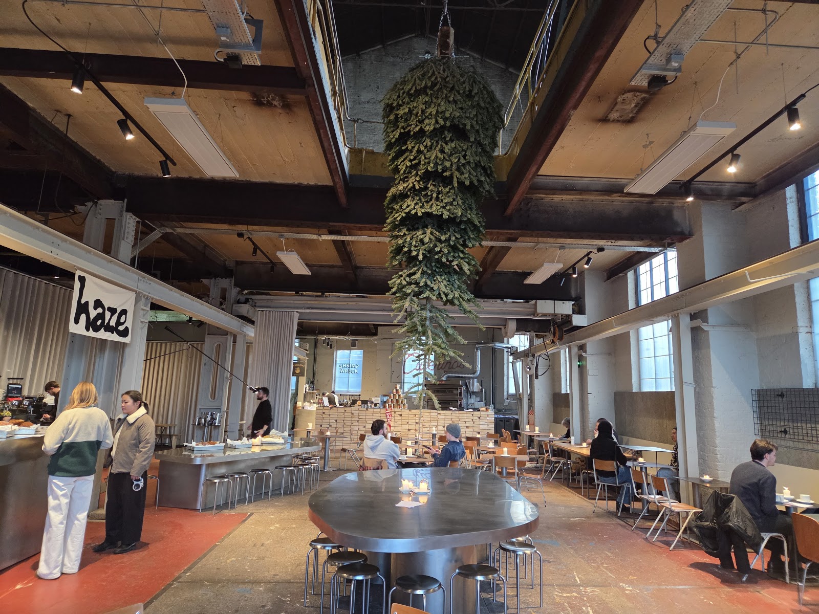 The hall at Brown's of Leith under its timber roof, with the Haze counter on the left, a round steel table and people at tables by the tall windows.