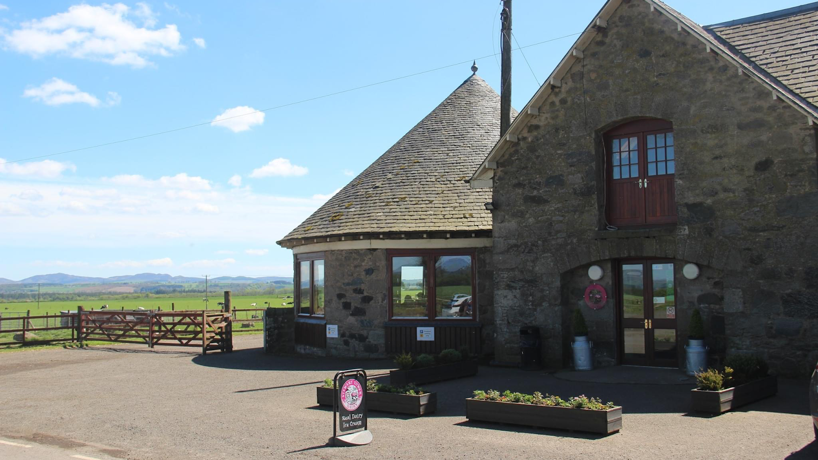 The round stone café and ice cream parlour at Stewart Tower Dairy on a sunny day, with farm fields and the Perthshire hills behind.