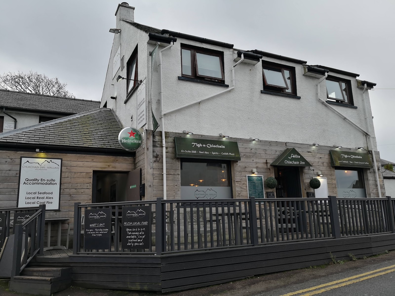 The Chlachain Inn in Mallaig, a pale two-storey inn with a timber terrace and picnic benches by the road.