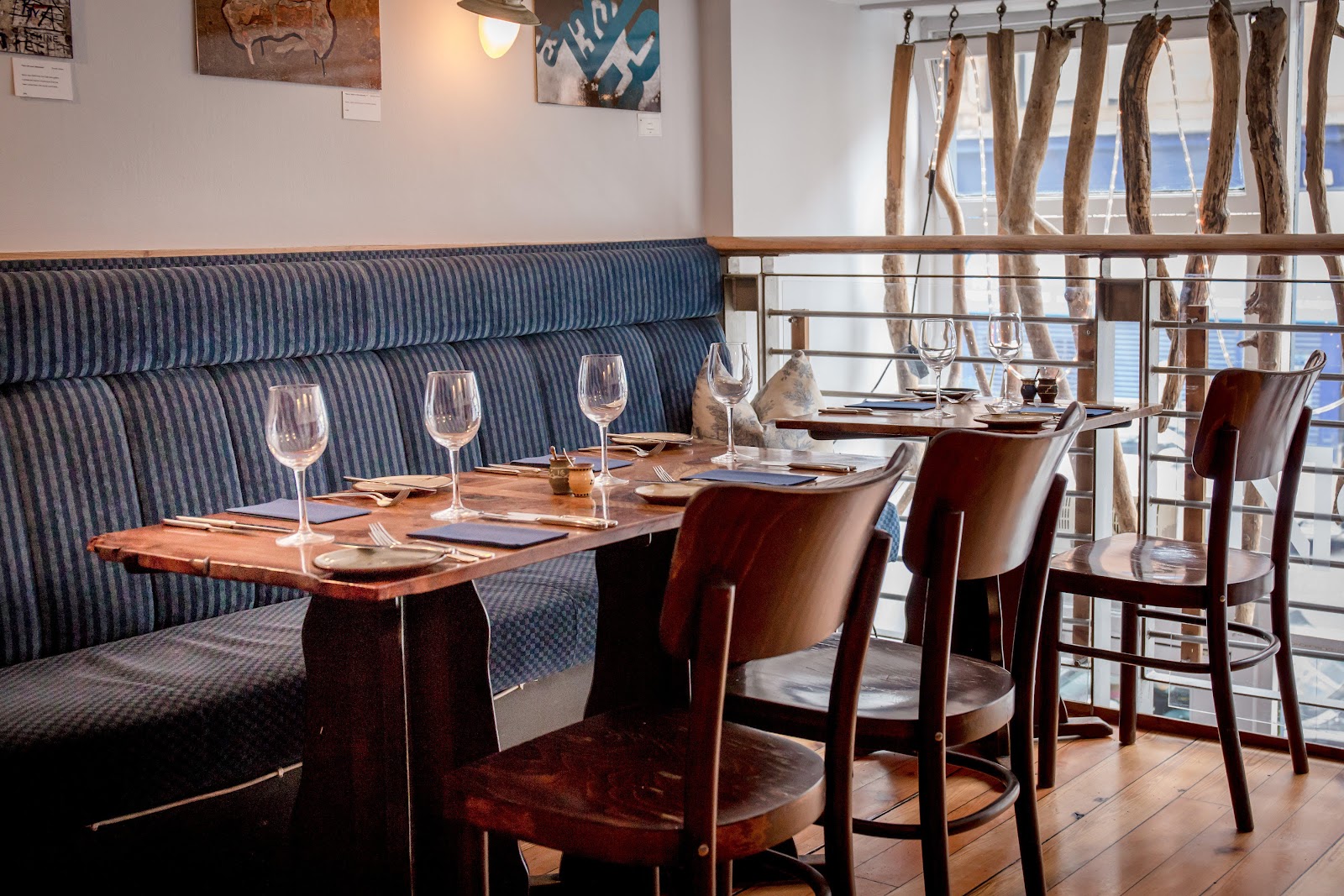 Tables laid on the upper level at Number 16, with a blue banquette and driftwood across the windows.