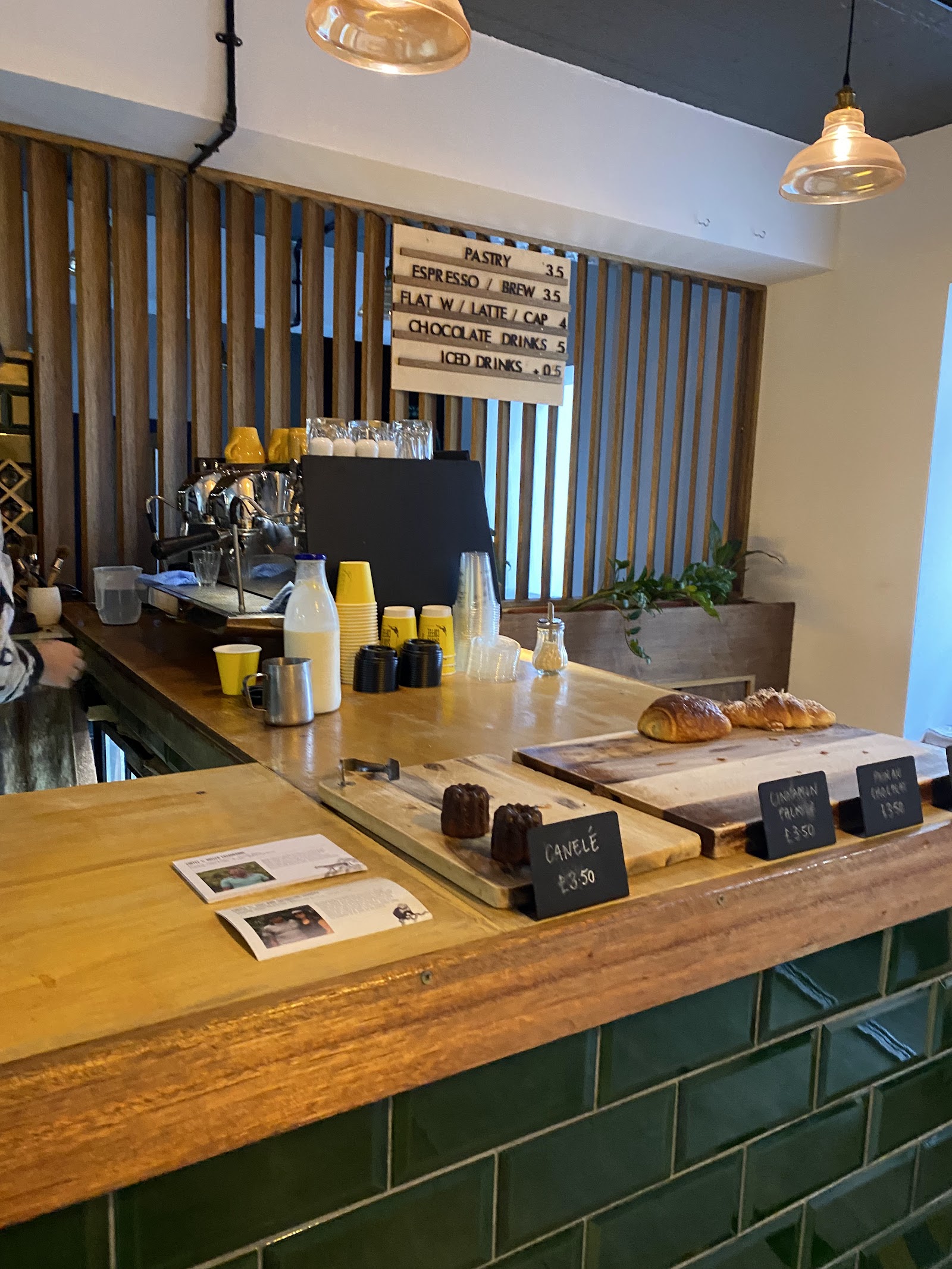 The counter at Santu on the Canongate, green tiles below and an espresso machine behind, with canelés and croissants on wooden boards.