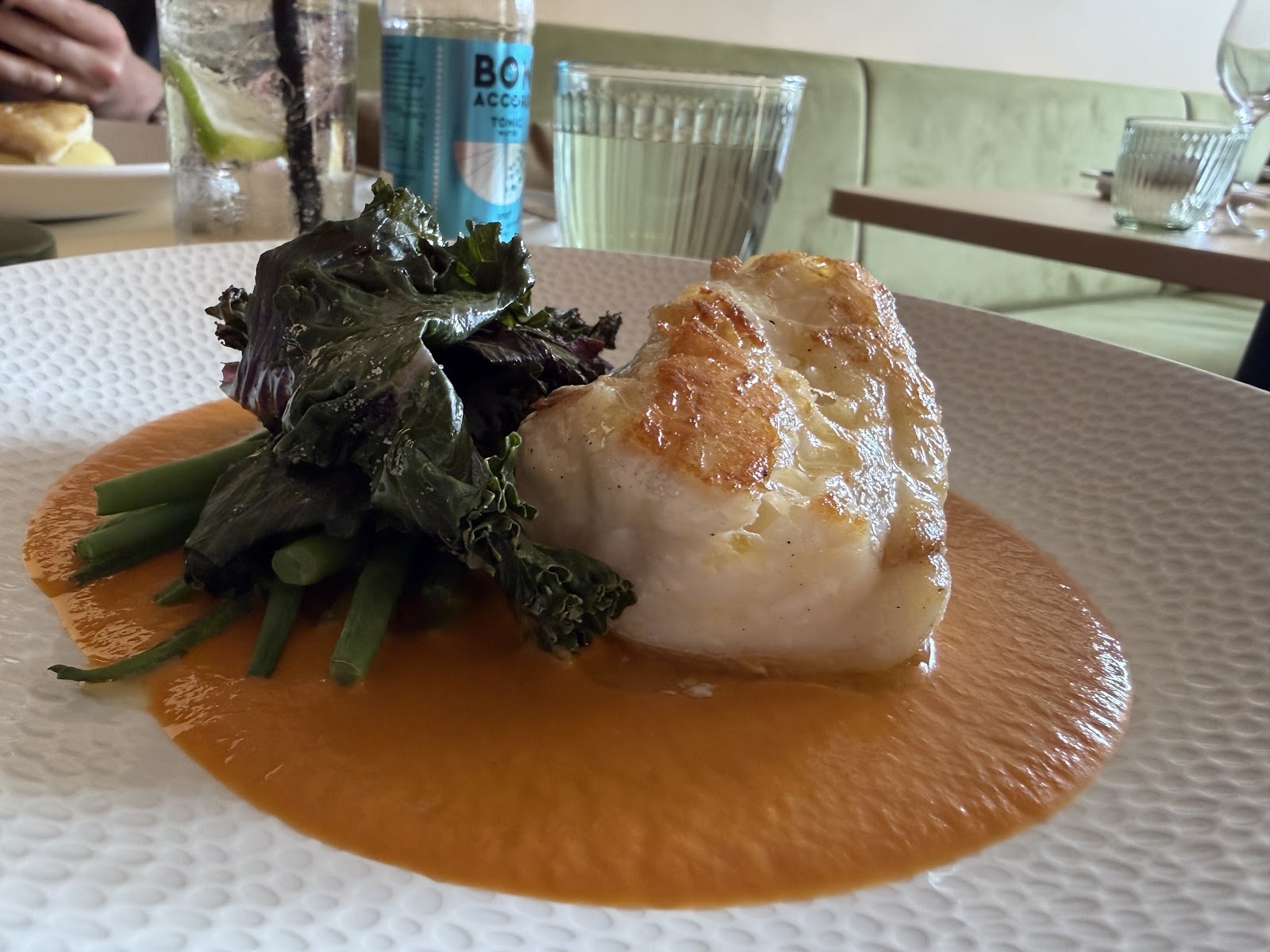 A fillet of fish on greens and green beans in an orange sauce, on a white plate at a table at Barry Fish.