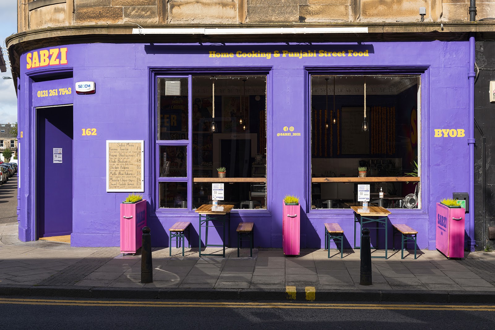 The purple corner front of Sabzi at 162 Ferry Road, signed Home Cooking and Punjabi Street Food, with benches and pink planters on the pavement.