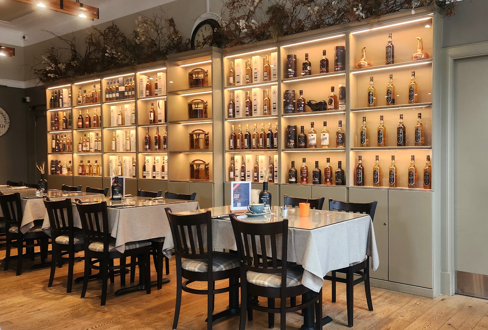 The dining room at The Bank in Huntly, a wall of lit shelves of whisky above tables laid with linen.
