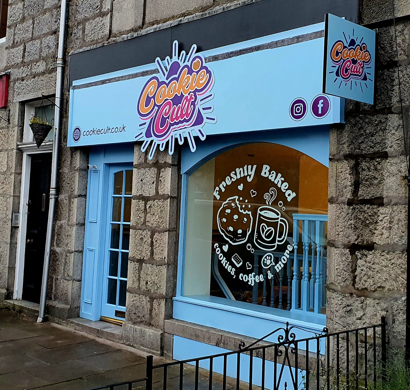 Cookie Cult's pale blue shopfront on St Swithin Street, with its bright logo over the door and Freshly Baked written across the arched window.