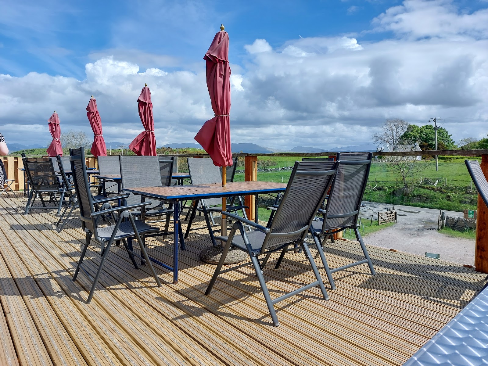 The café's timber deck with tables and red parasols, looking out over green fields to the hills.