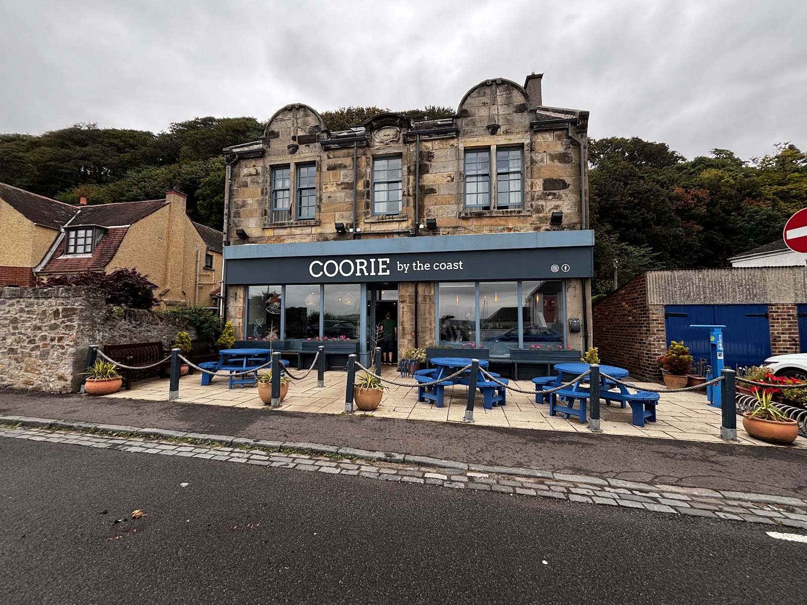 Coorie by the Coast in Limekilns, a stone building with a blue cafe front and picnic tables outside.