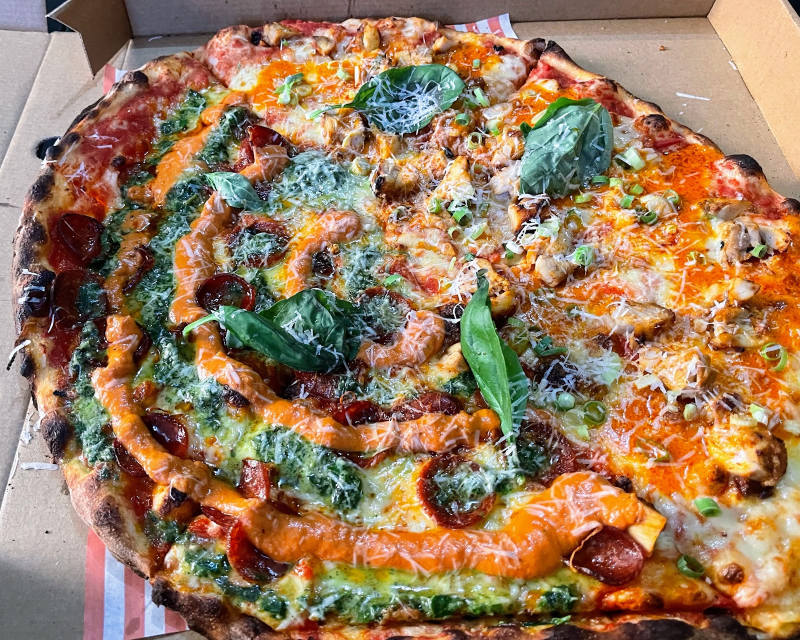 A whole thin-crust pizza with pepperoni, pesto, basil and a drizzle of sauce, in its box from Anxious Pete's.